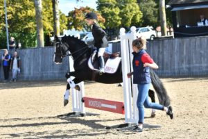 Young girl on horse jumping over a low jump with helping running alongside