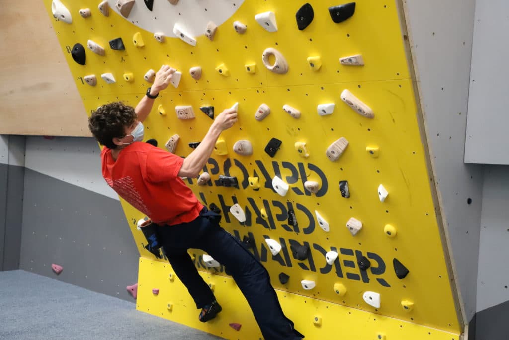 Boy dressed in red tshirt and navy trousers, climbing on a yellow wall