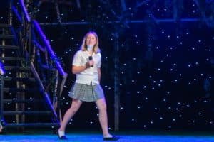 Girl in blouse and skirt on stage holding microphone